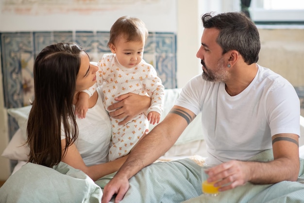 Family with baby sitting together in bed in morning