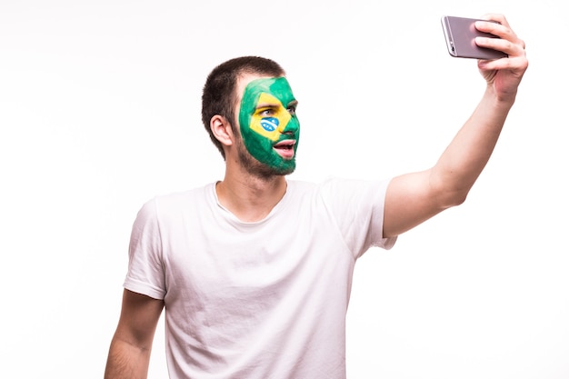 Fan support of Brazil national team take selfie on the phone with painted face isolated on white background