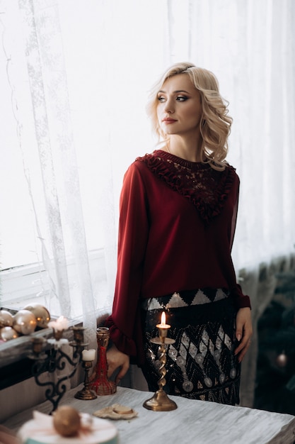 Free photo fancy blonde woman dressed in red clothes stands in a room with christmas decor