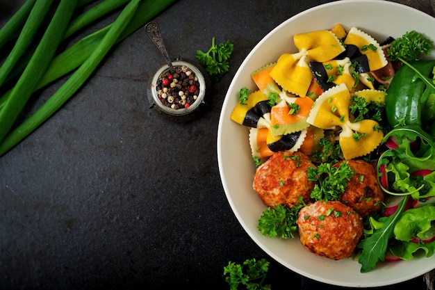 Farfalle pasta durum wheat with baked meatballs of chicken fillet  in tomato sauce and salad in  bowl.