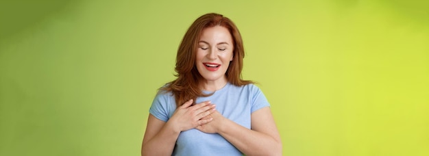 Free photo fascinated cute redhead passionate middleaged woman sighing lovely touch heart close eyes smiling delighted express admiration temptation feeling appreciation grateful emotions green background