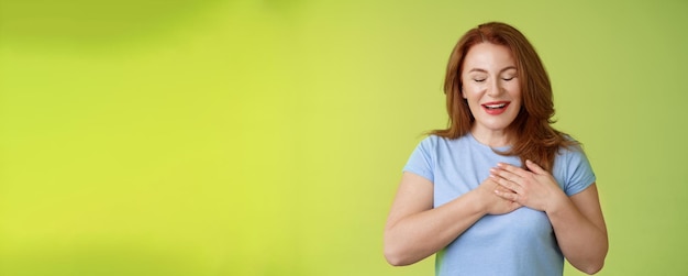 Free photo fascinated cute redhead passionate middleaged woman sighing lovely touch heart close eyes smiling delighted express admiration temptation feeling appreciation grateful emotions green background