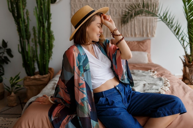 Free photo fascinating brunette woman in straw hat chilling at home in cozy boho interior