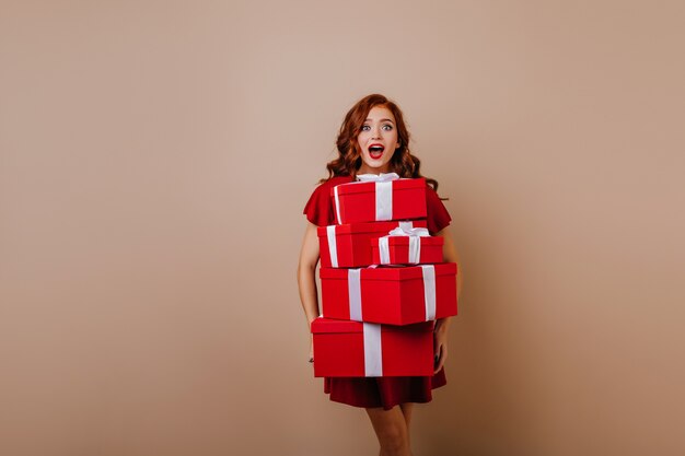 Fascinating giner young woman holding christmas presents. Indoor photo of stunning girl posing with surprised smile in new year.