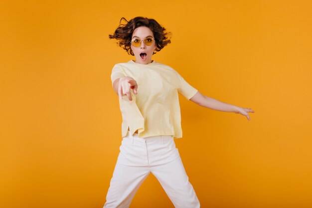 Free Photo fascinating pale girl posing with shocked face expression ansd mouth open. spectacular young lady in orange sunglasses and yellow t-shirt expressing amazement.