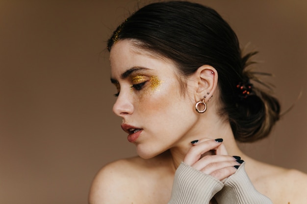 Free photo fascinating woman with party makeup posing . indoor close-up photo of relaxed brunette girl wears earrings.