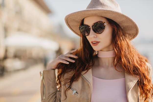 Fascinating young lady with long hairstyle looking around through sunglasses