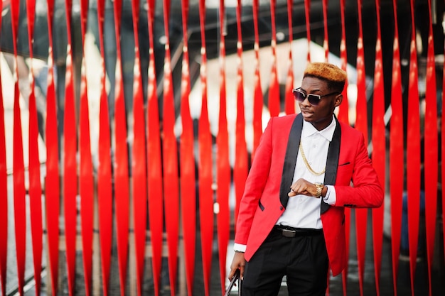 Fashion african american man model at red suit with highlights hair and handbag posed at street and looking at his watches