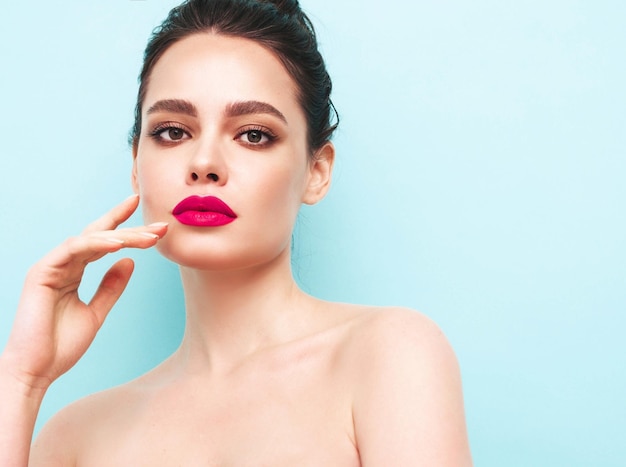 Fashion beauty portrait of young brunette woman with evening stylish makeup and perfect clean skin Sexy model with hair in a bun posing in studio near blue wall With pink bright natural lips