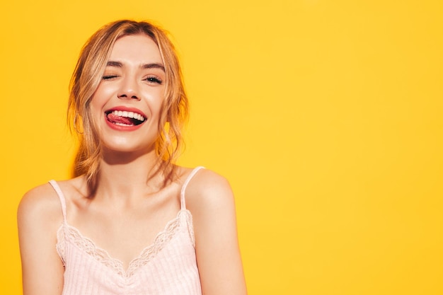 Fashion beauty portrait of young brunette woman with natural stylish makeup and perfect clean skin Sexy model with long curly hair posing in studio on yellow background shows tongue Winks