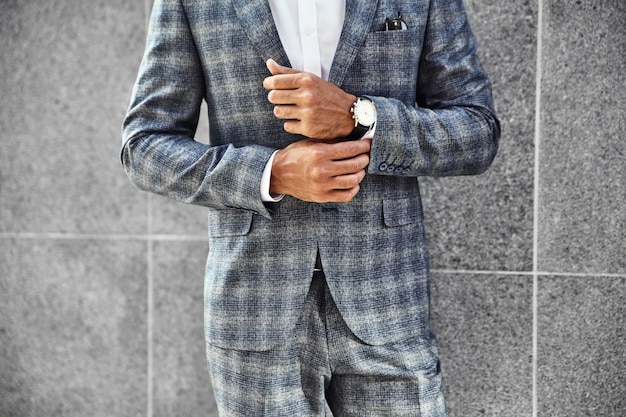 Free photo fashion businessman model dressed in elegant checkered suit posing near gray wall on street background. metrosexual with luxury watch on wrist