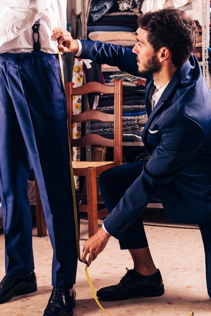 Fashion designer taking measurement of male customer's pant in the shop