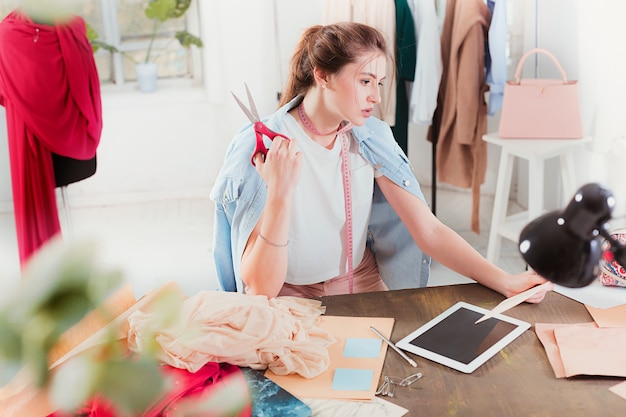 Free photo fashion designer woman working in studio sitting on the desk