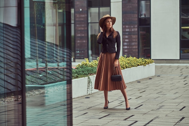 Free photo fashion elegant woman wearing a black jacket, brown hat and skirt with a handbag clutch walking on a european city center.