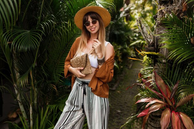 Fashion  image of  sexy graceful  woman in straw hat posing on tropical palm leaves