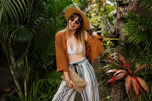 Fashion  image of  sexy graceful  woman in straw hat posing on tropical palm leaves