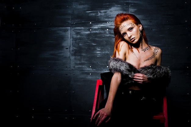 Free photo fashion model red haired girl with originally make up like leopard predator against steel wall studio portrait on ladder