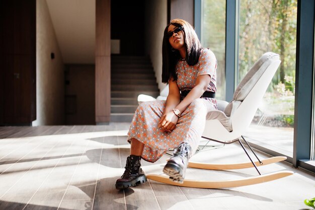 Fashion portrait of african american woman in long dress boots and sunglasses indoor