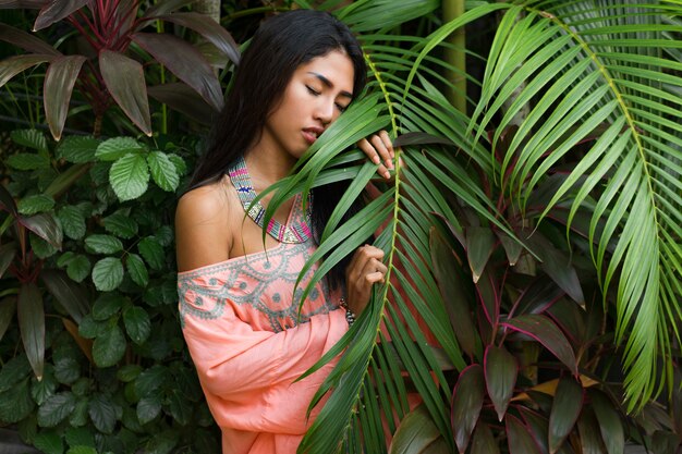 Fashion portrait of attractive asian woman posing in tropical garden. Wearing boho dress and stylish accessories.