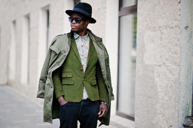 Fashion portrait of black african american man on green velvet jacket black hat and coat cloak on his shoulders walking on streets of city background house with many windows