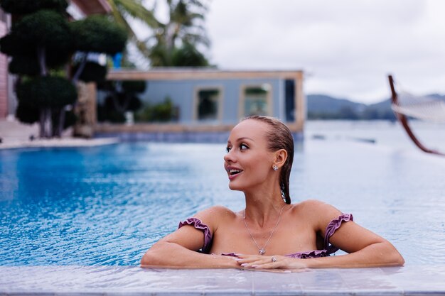 Fashion portrait of caucasian woman in bikini in blue swimming pool on vacation at coudy day natural light