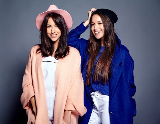 fashion portrait of two smiling brunette women models in summer casual hipster overcoat posing on gray