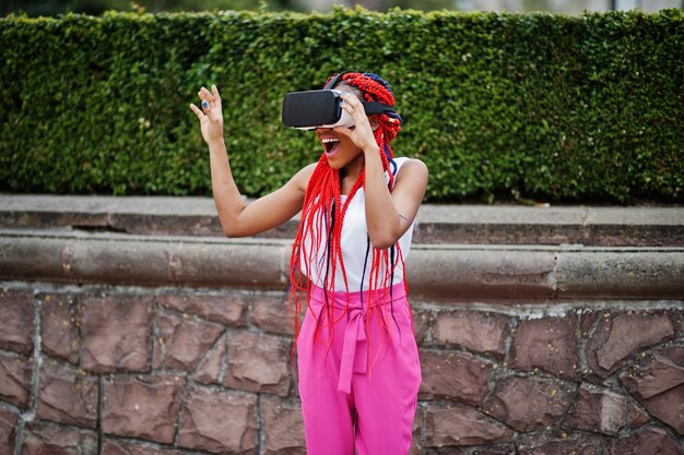 Fashionable african american business woman at pink pants and red dreads with virtual reality glasses outdoor