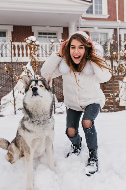 Free Photo fashionable amazing woman having fun with cute husky dog outdoor in snow. happy winter time of real friends, home pets, love animals