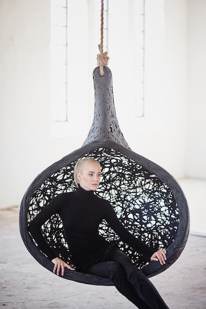 Free photo fashionable blond female sits on a round chair in a big empty room.