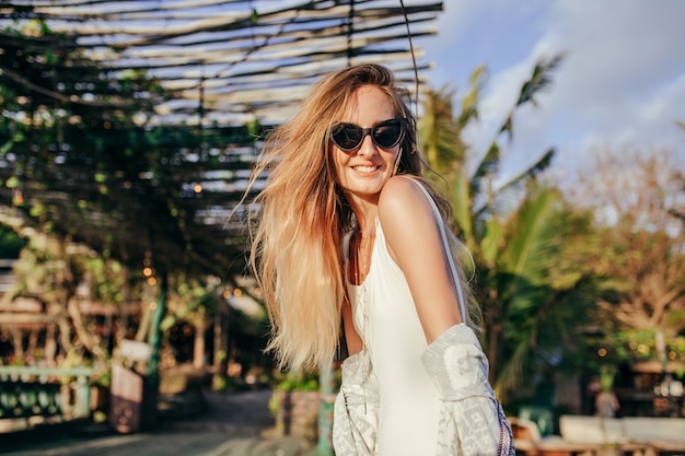 Fashionable blonde woman in white swimwear in exotic place