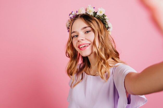 Fashionable woman in flower wreath making selfie with gently smile