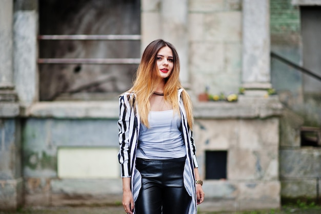 Fashionable woman look with black and white striped suit jacket leather pants posing at old street Concept of fashion girl