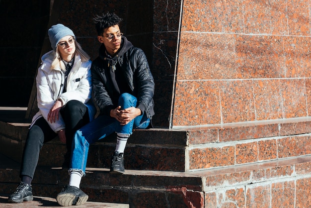 Fashionable young interracial couple sitting on steps looking away