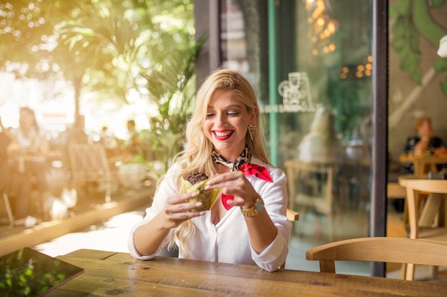 Free photo fashionable young woman sitting in the caf� eating muffin