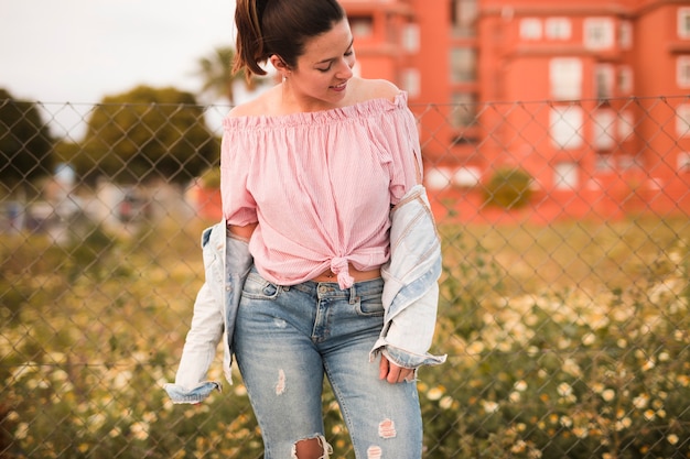 Free photo fashionable young woman standing in front of fence looking away