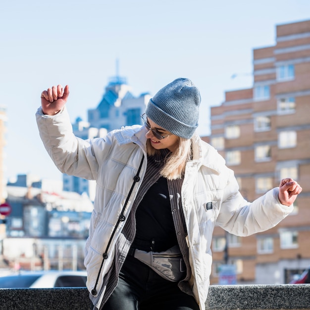 Fashionable young woman wearing blue knit hat dancing in the city