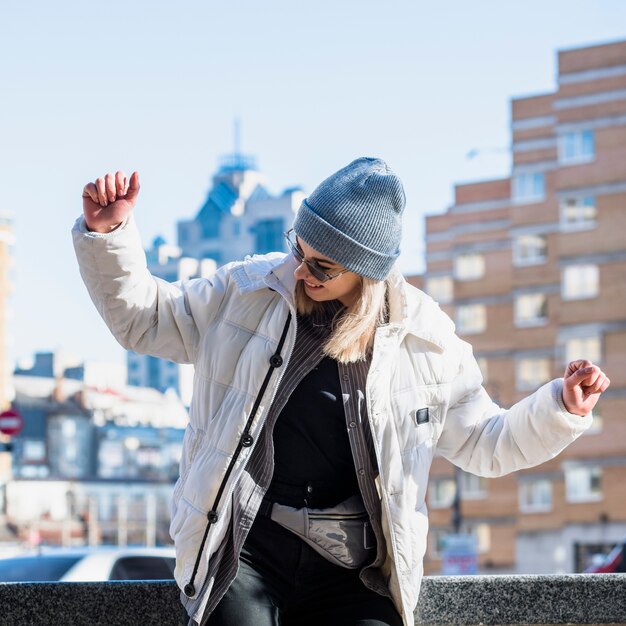 Fashionable young woman wearing blue knit hat dancing in the city