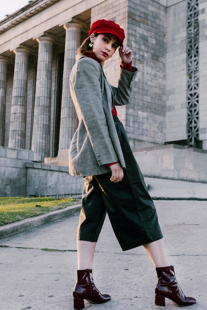 Fashionable young woman with hand on her red cap looking at camera