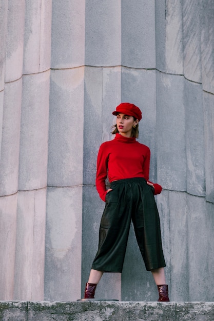 Fashionable young woman with her hands in pocket standing in front of large pillar