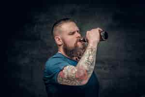 Free photo fat bearded men with tattoos on arm drinks beer from a bottle.