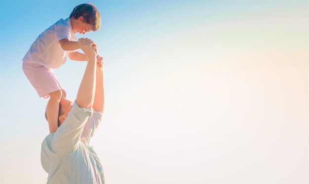 Father carrying his cheerful son on his shoulders with the bright sky