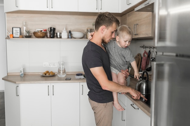 Father carrying his son showing something on kitchen counter