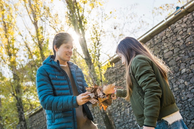 Free photo father and daughter holding dry autumn leaves in front of stone wall