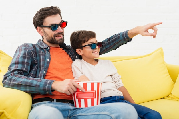 Free photo father holding popcorn and watching a movie with his son