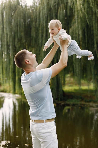 Father and little baby daughter standing in the park and posing for a photo. Family wearing white and light blue clothes