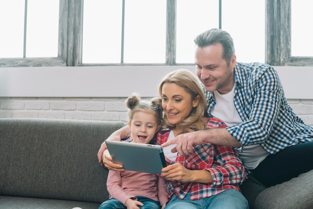 Father pointing on digital tablet with her smiling wife and daughter at home