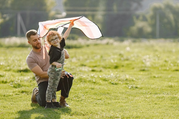 Free photo father and son playing with a kite and having fun on summer park outdoor curly toddler boy wearing a khaki overalls