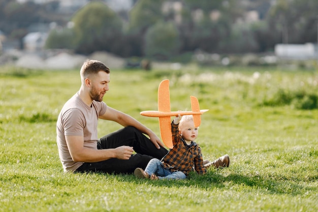 Free photo father and son playing with a plane toy and having fun on summer park outdoor curly toddler boy wearing jeans and plaid shirt