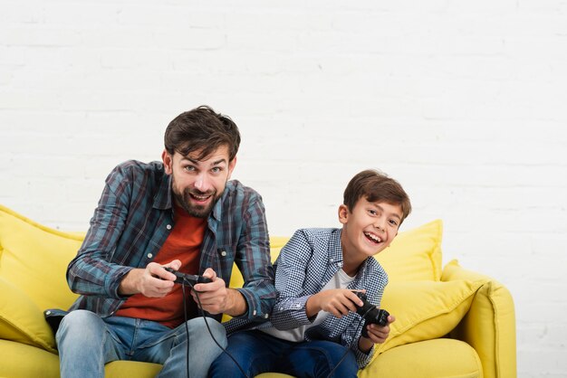 Father and son sitting on sofa and playing on console