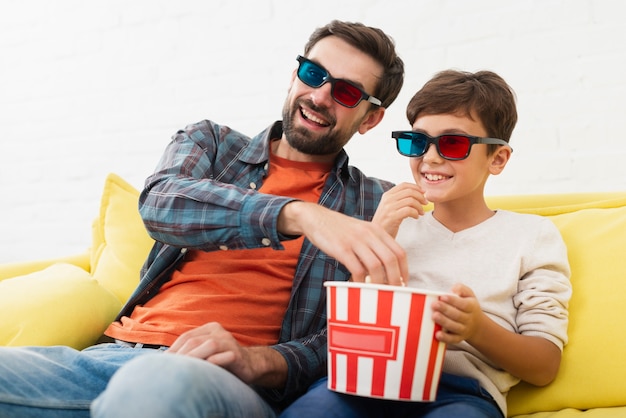 Free photo father and soon eating popcorn and watching a movie